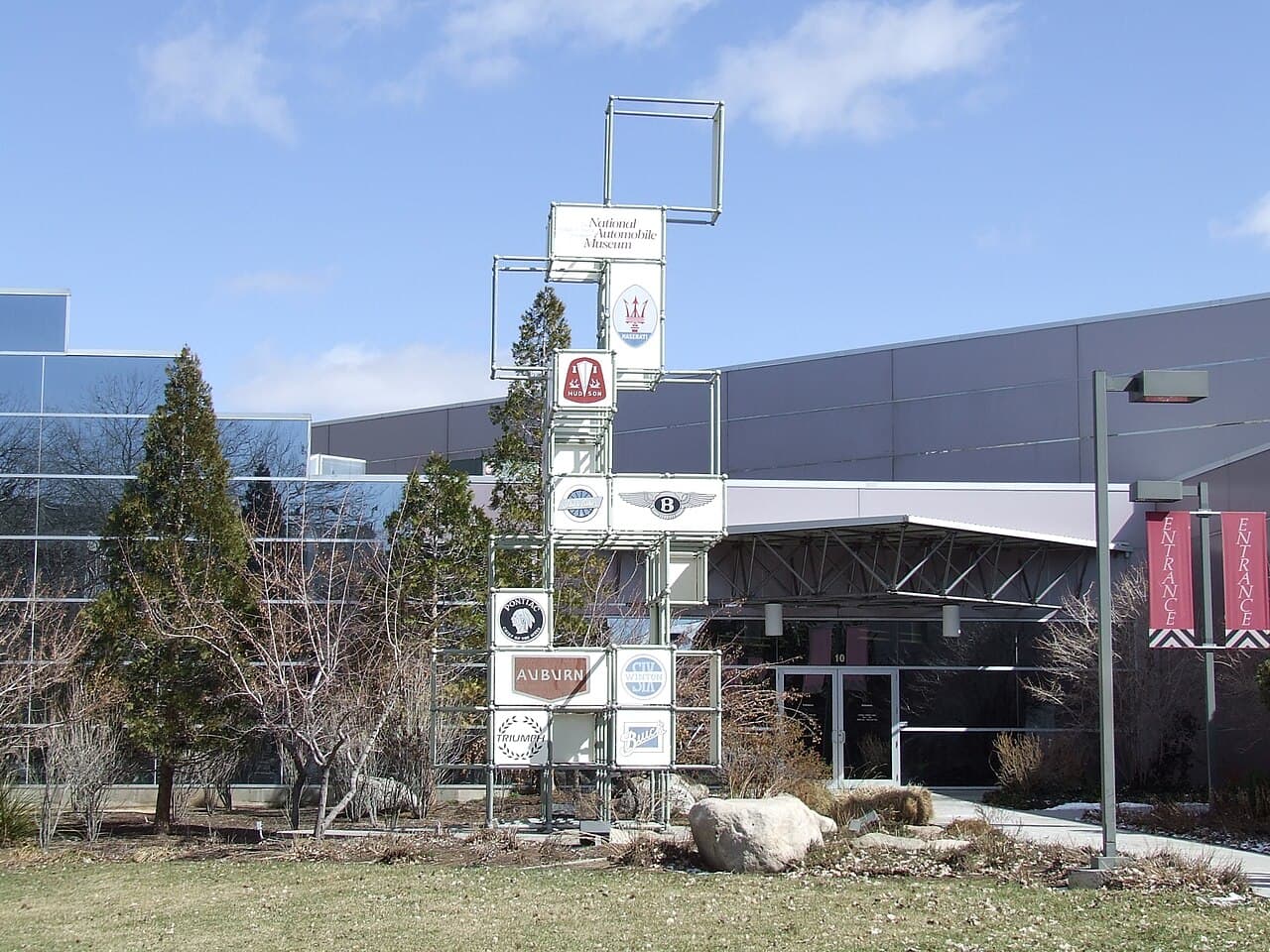 Entrance sign and modern exterior of the National Automobile Museum in Reno, Nevada, with manufacturer badges mounted on a tall metal frame.